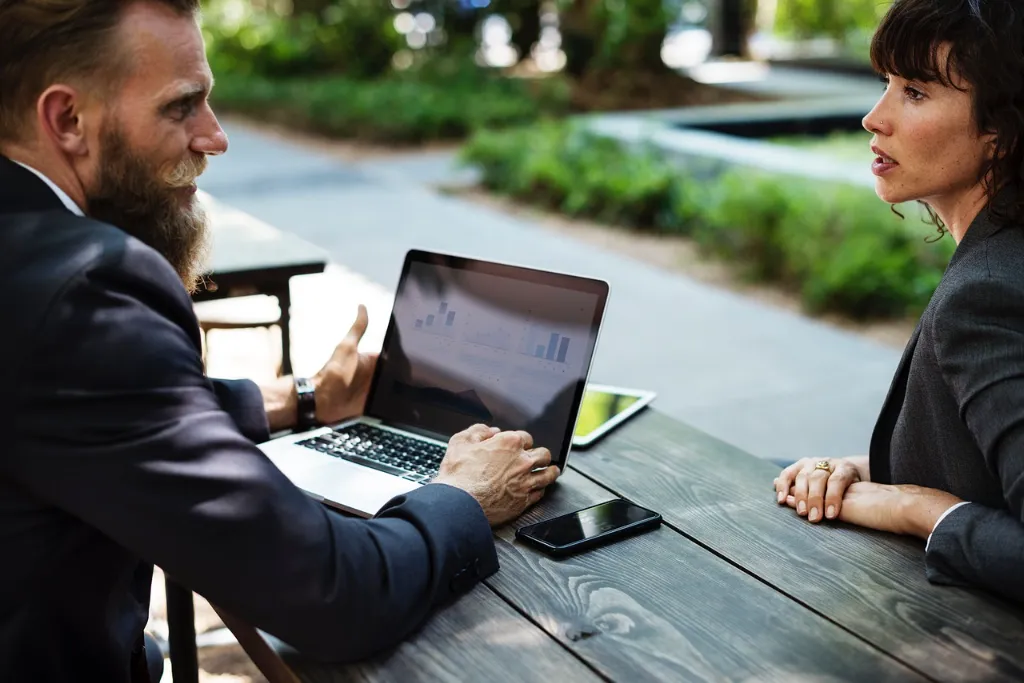 A man and woman working on a laptop outside.