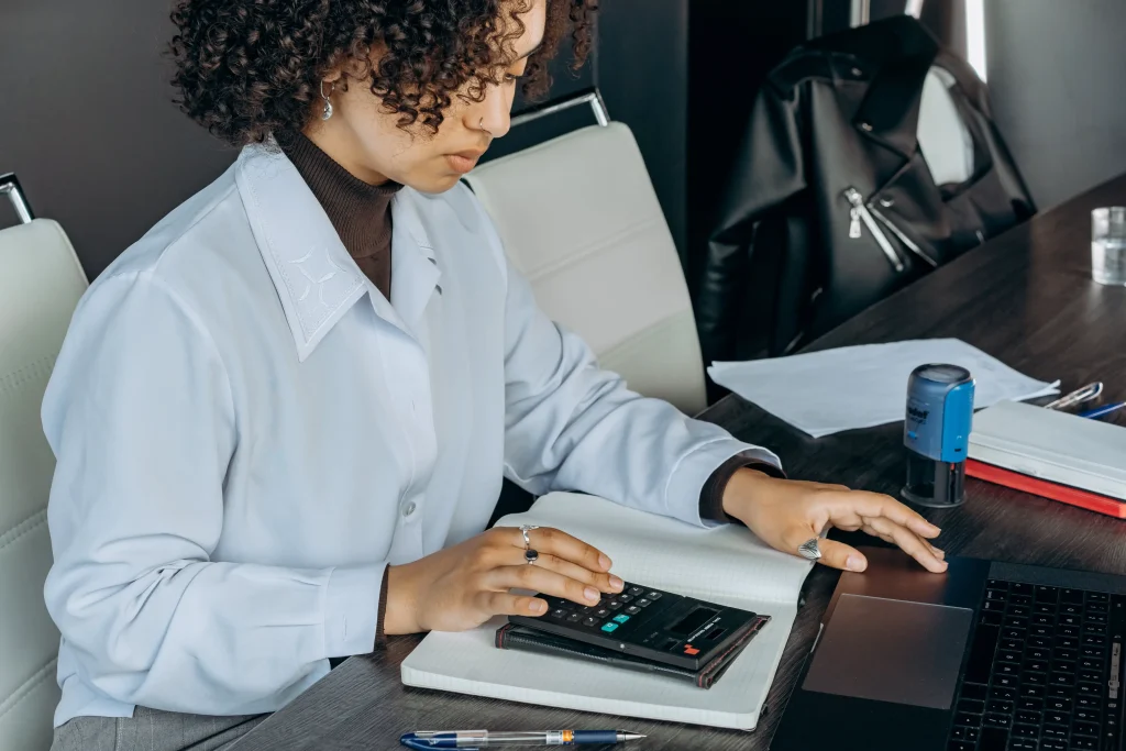 A woman working overtime at a her laptop with a calculator.