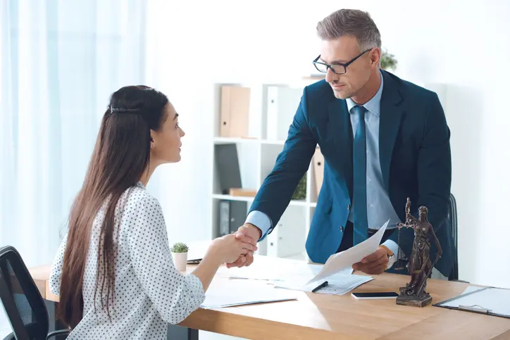 Two employees shaking hands over a desk.