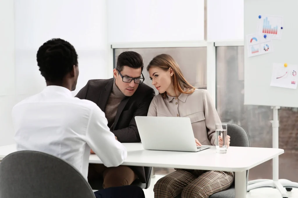 A black man interviewing for a job with two white employers talking to each other.