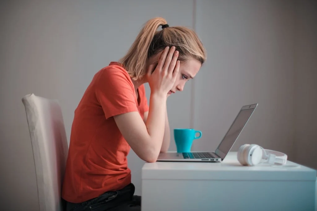 A concerned woman sitting at her desk looking down at her laptop.