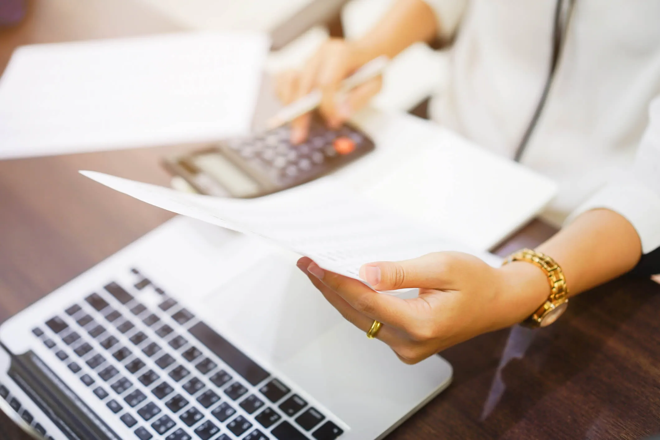 A woman reviewing paperwork with her computer and calculator.