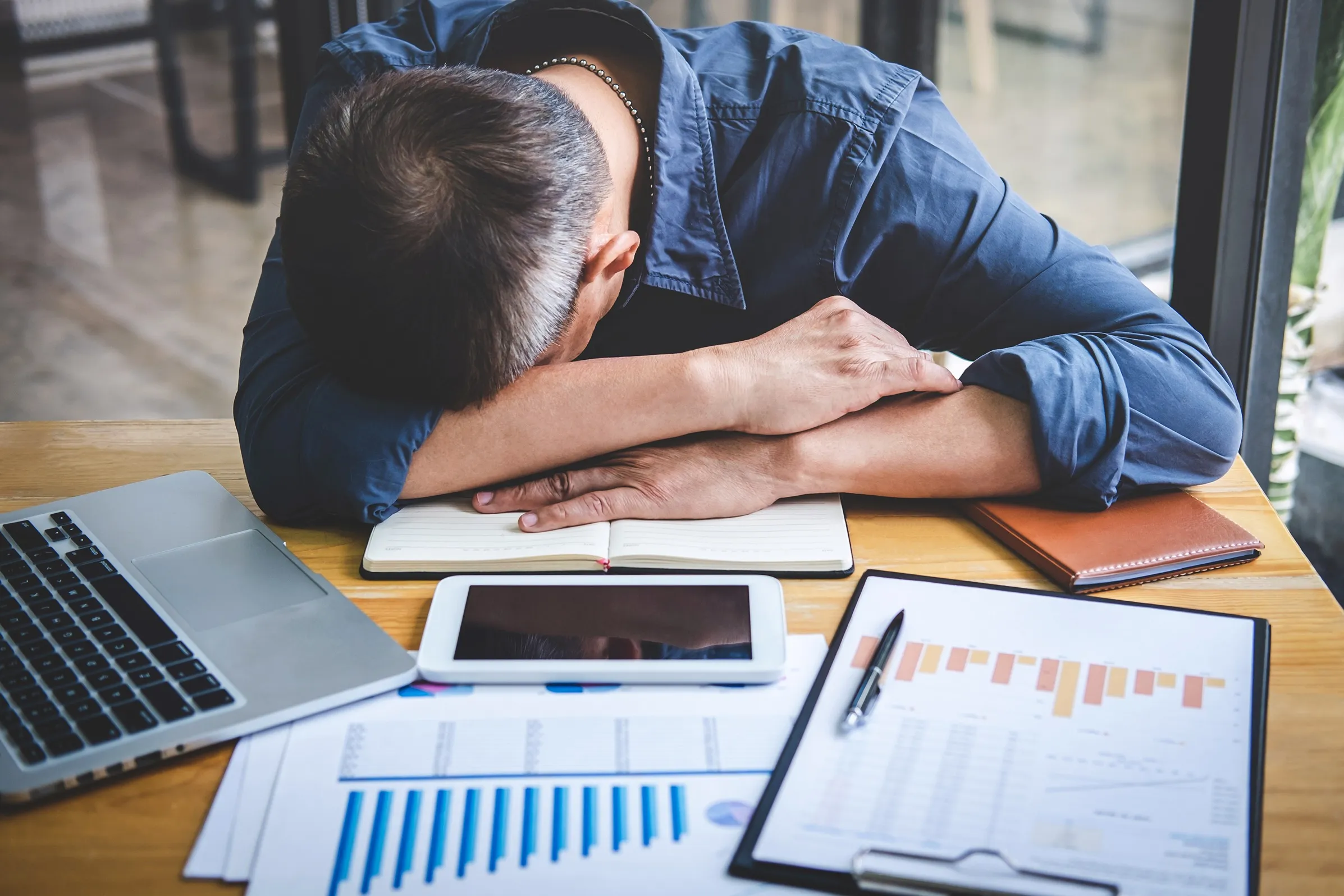 A distressed man with his head down on his desk at work.
