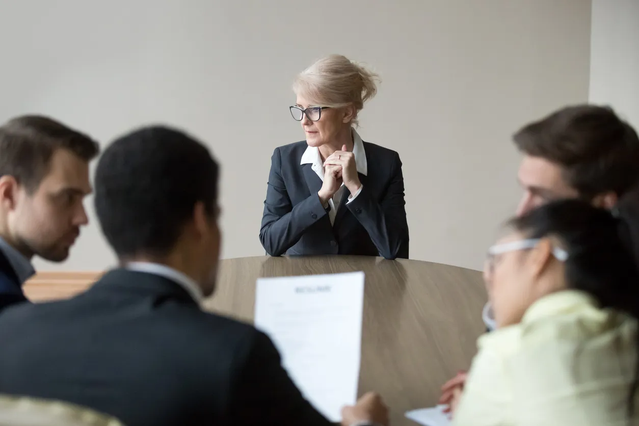 An elderly employee sitting at a table with other employees.